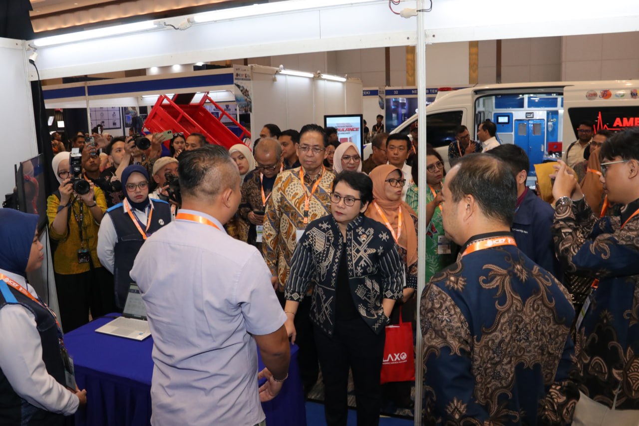 Pengunjung berbincang di area stan pameran dengan kendaraan layanan kesehatan di latar.