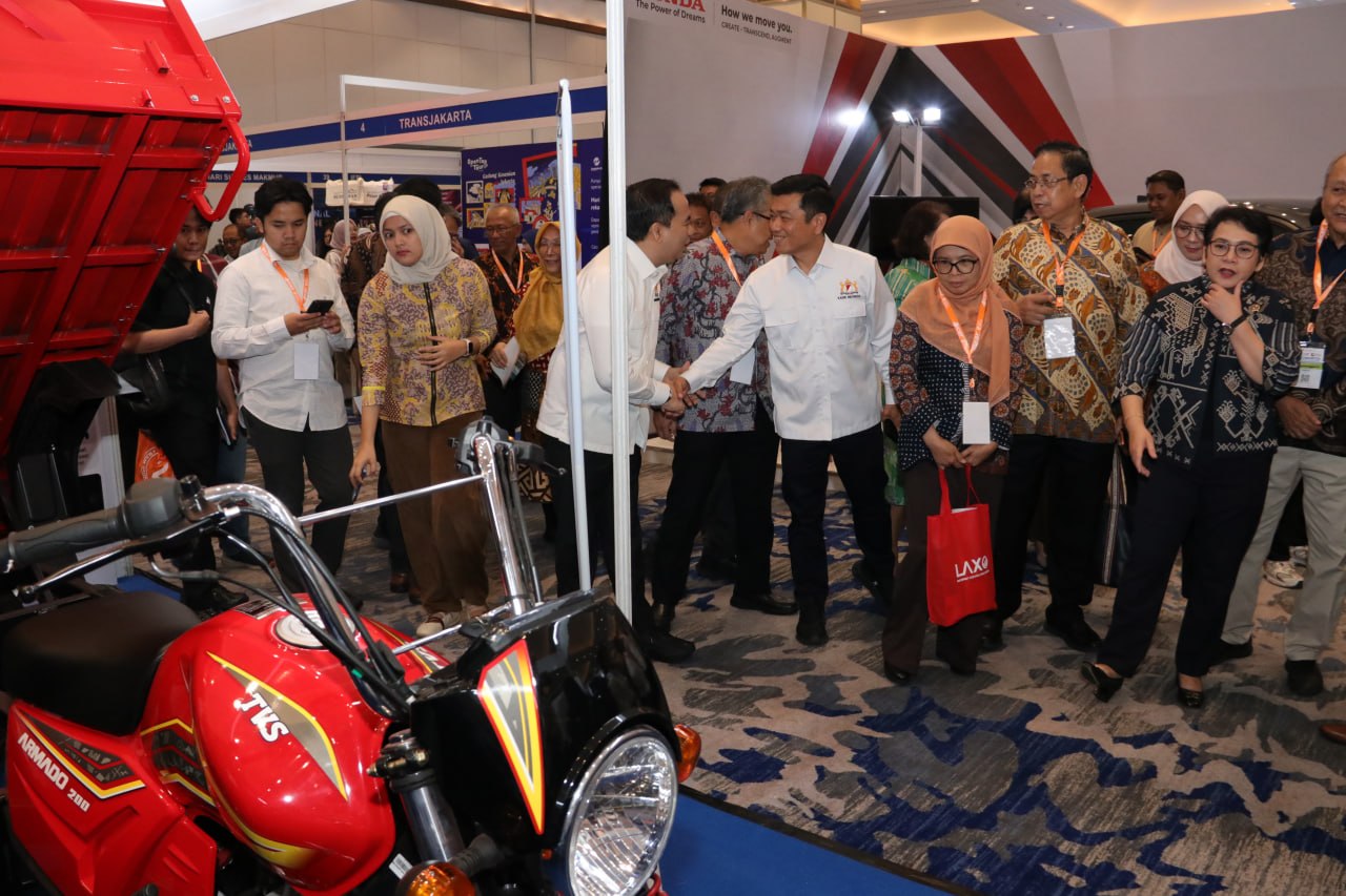 Pengunjung berada di dekat kendaraan niaga merah yang dipamerkan di dalam ruangan.